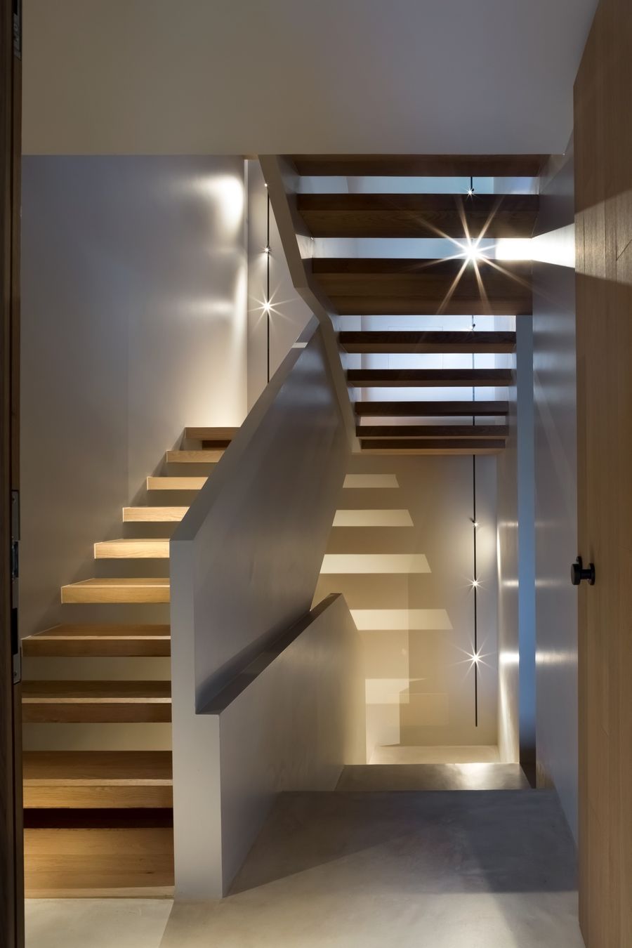 La scala interna di Casa LAGO Dolomiti con gradini in legno a sbalzo e illuminazione puntuale