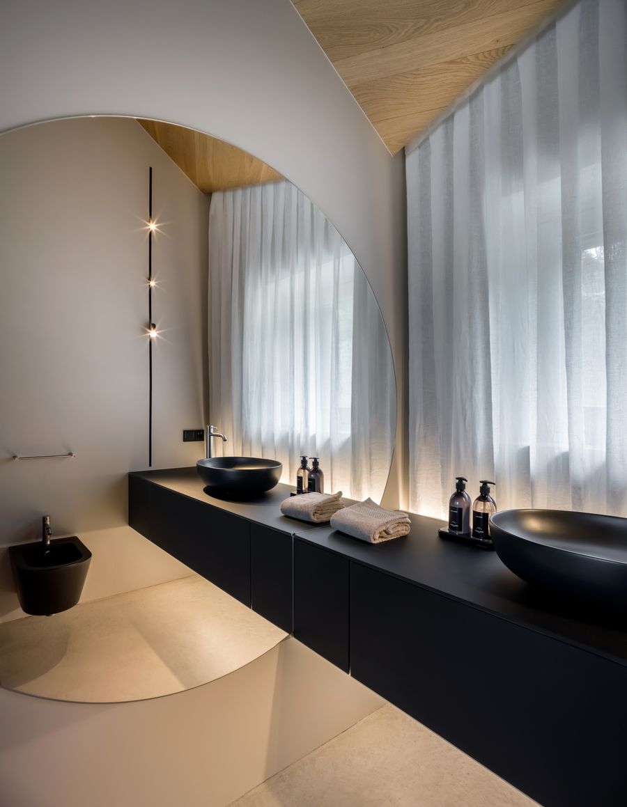 Il bagno di Casa LAGO Dolomiti con mobile sospeso scuro, lavabi a bacile e tenda plissettata